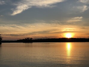 Un lago tranquilo al atardecer, con cielo despejado y la silueta de árboles en el fondo.