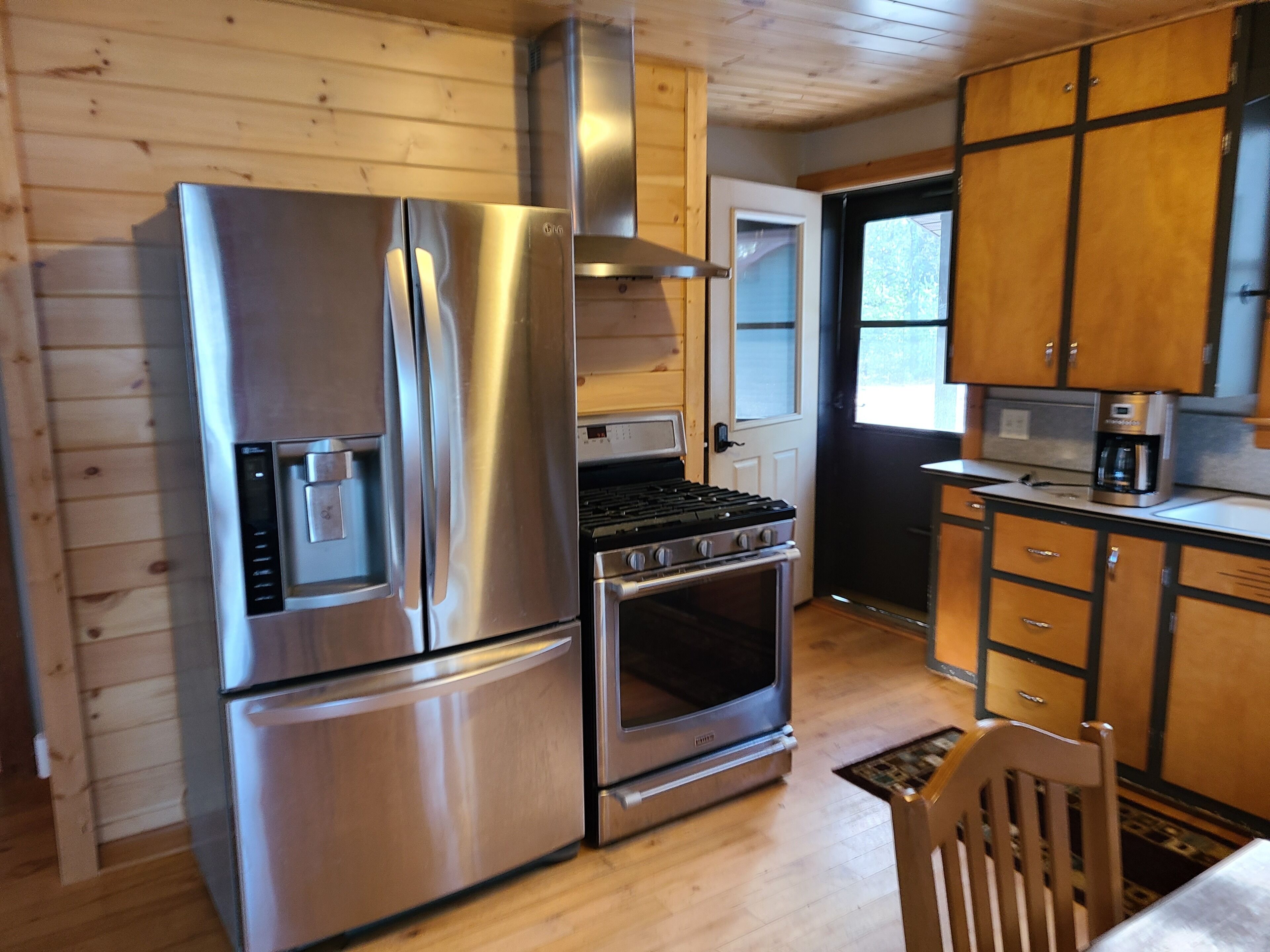 A compact kitchen with stainless steel appliances, wooden cabinets, and a window providing natural light.