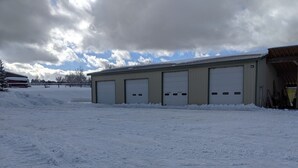 A large industrial building with multiple garage doors, a snow-covered ground, and a cloudy sky. - Nice apartment in shop with Indoor parking for toy trailers or vehicle. (THAYNE)
