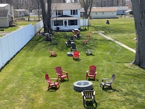 A backyard with a white fence, a covered patio, and several Adirondack chairs.