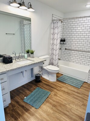 Une salle de bain moderne avec des toilettes blanches, un lavabo avec un miroir, une douche avec un rideau à motifs et une baignoire.