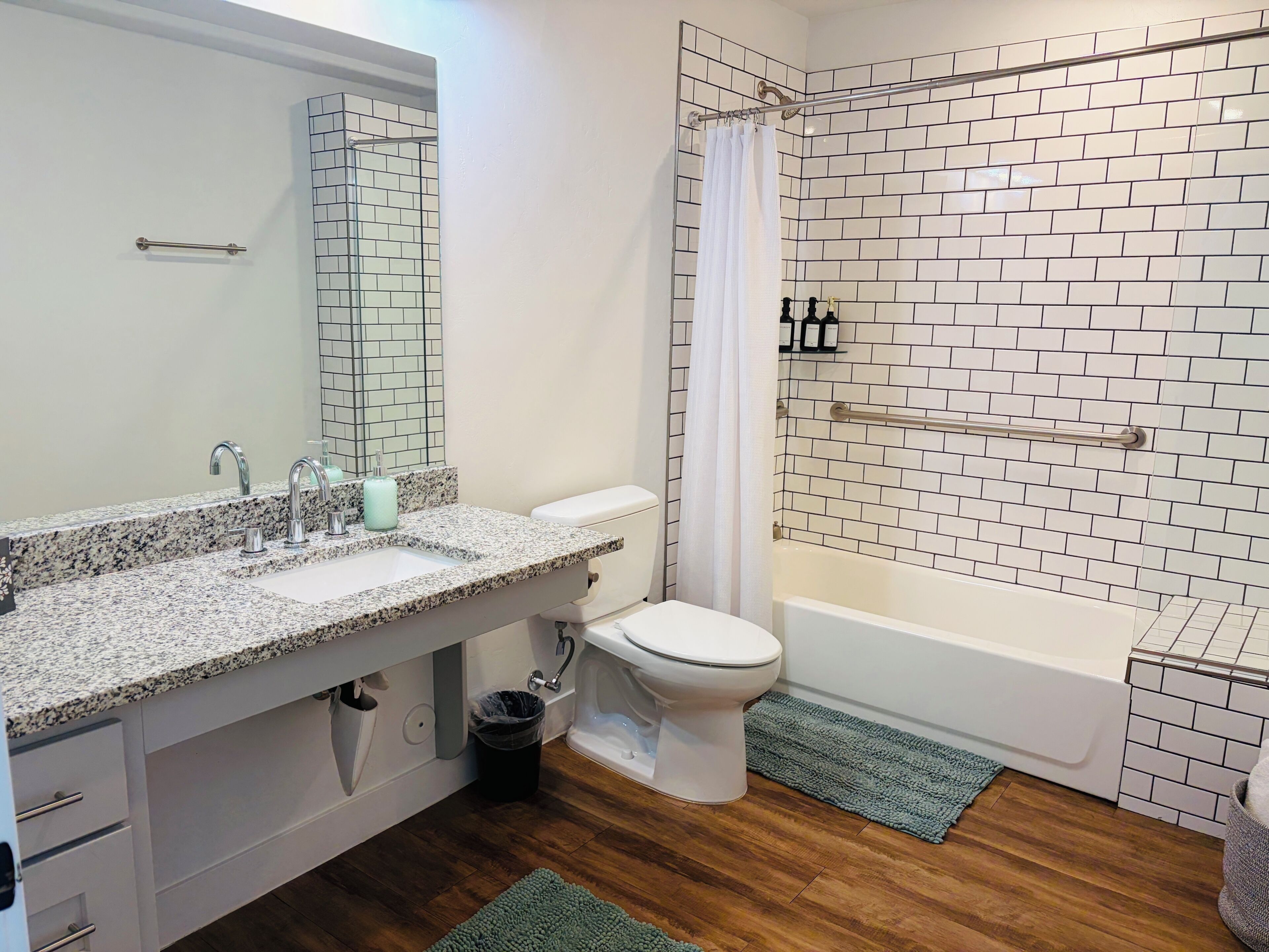 A bathroom with a granite countertop sink, a white toilet, a bathtub, and a shower with a white curtain.
