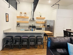 A modern kitchen with a central island, bar stools, a refrigerator, and a dining area with a table and chairs.