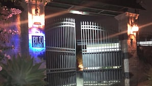 A gated entrance with a neon sign reading "BLU BAMBU" and a dog walking towards the gate.