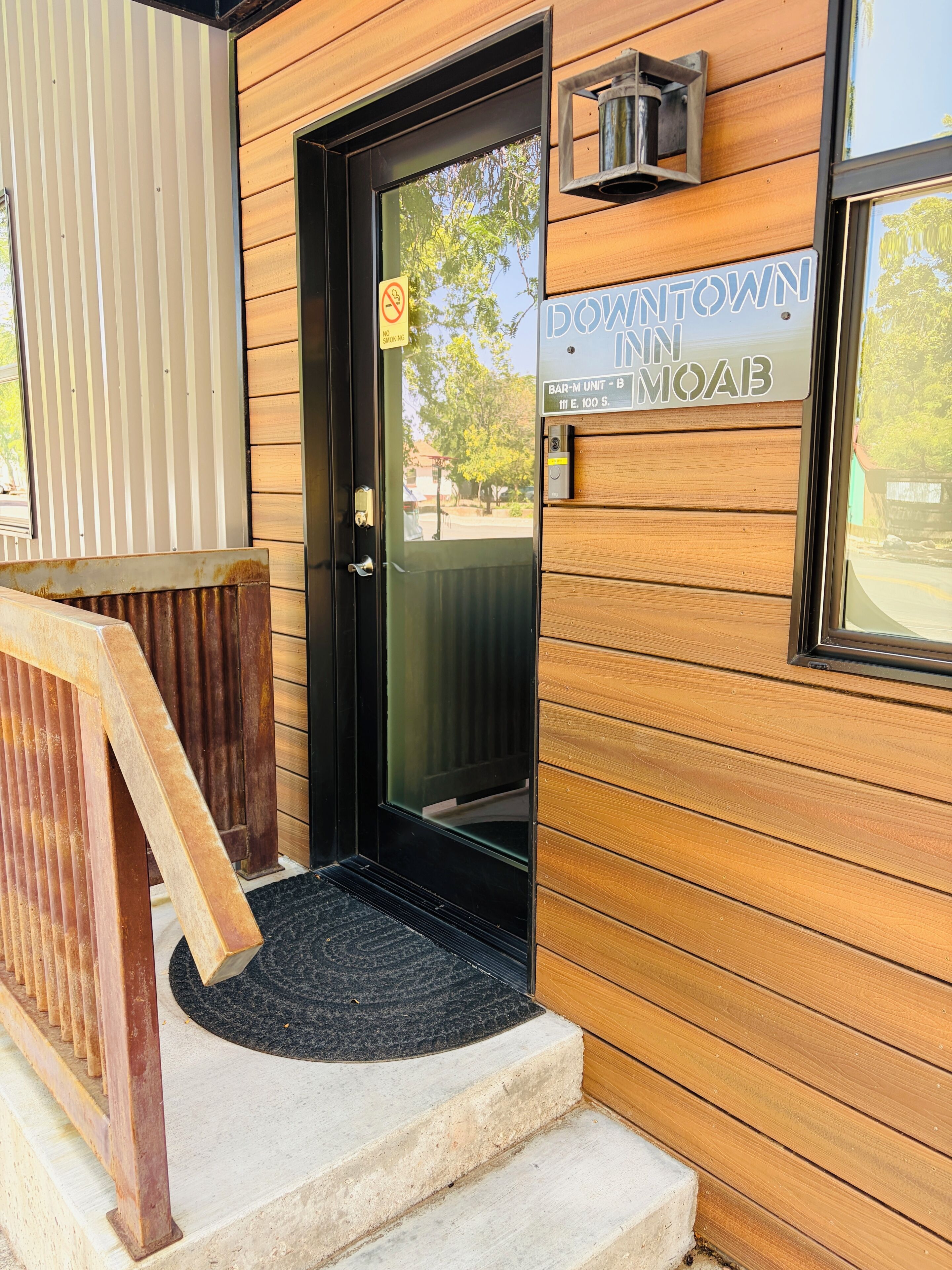 A wooden building with a black door, a sign reading 'Downtown Inn Moab,' and a small outdoor seating area with a wooden bench.