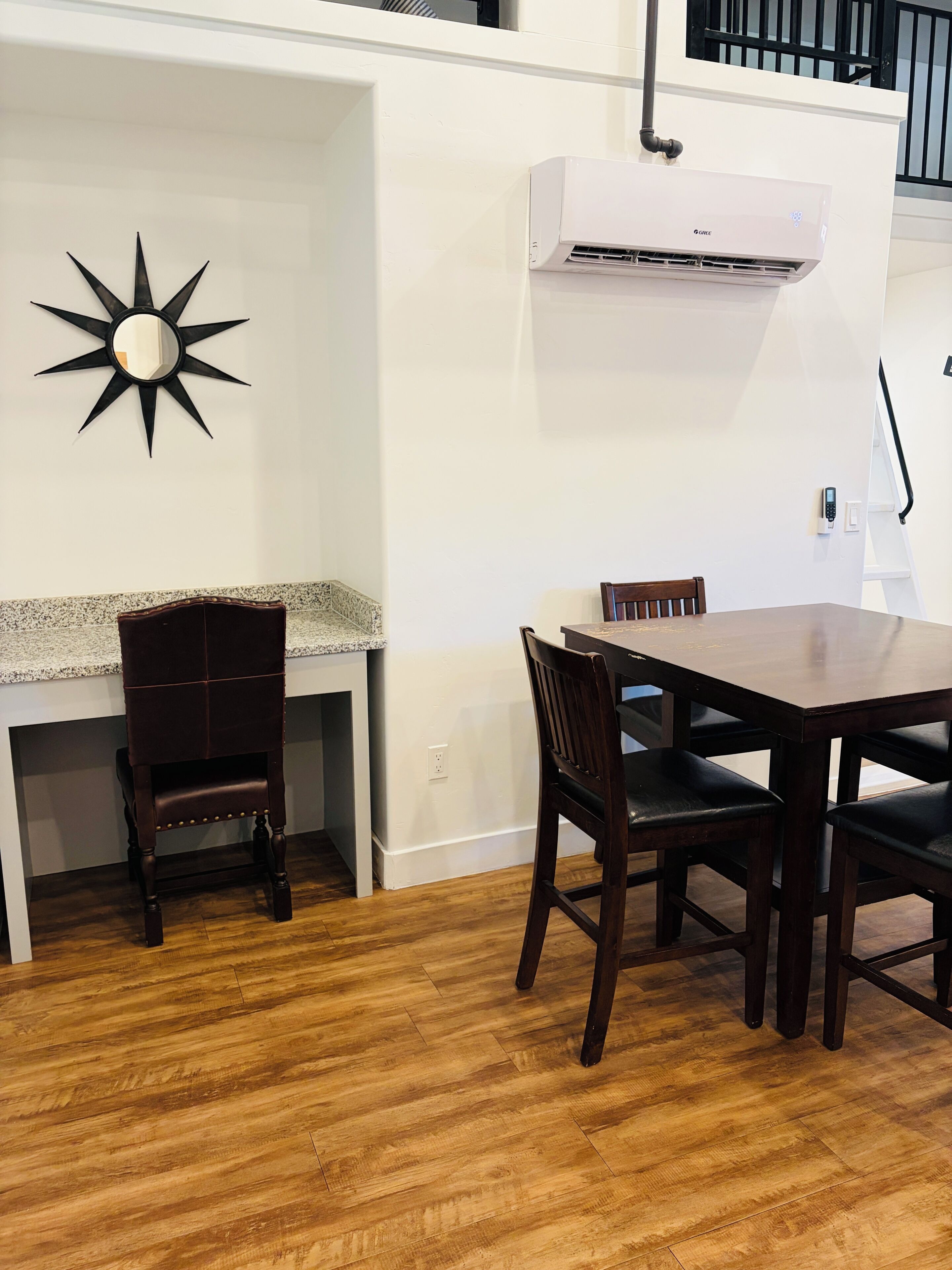 A dining area with a wooden table and chairs, a wall-mounted air conditioner, and a star-shaped mirror.