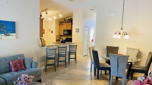 A modern living room with a sofa, a coffee table with a vase, and a dining area with chairs and a table. -  SandyRidge Five bedroom villa pool and spa home with no rear neighbors (Davenport)