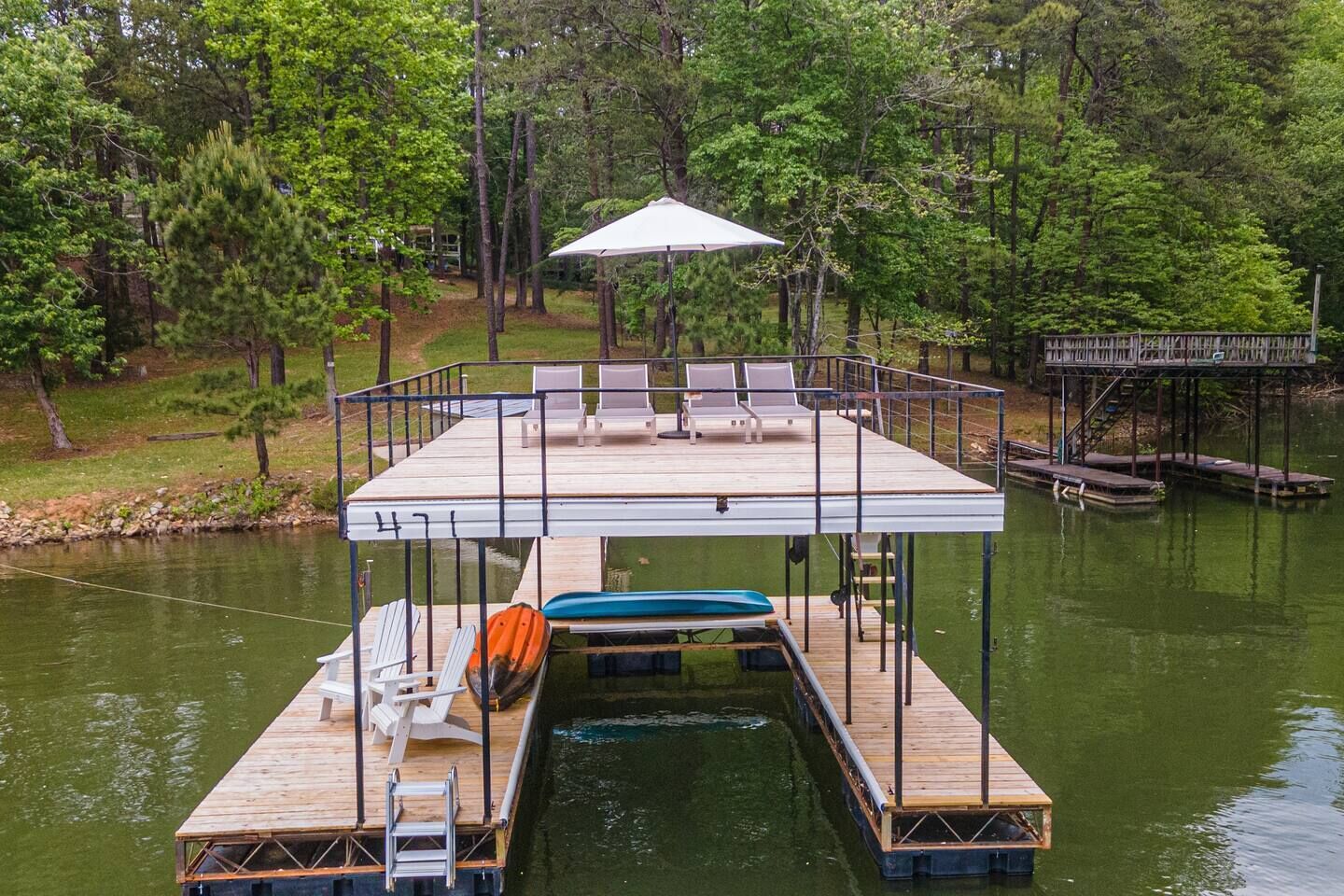 A wooden dock with a covered seating area, a boat, and a small bridge.