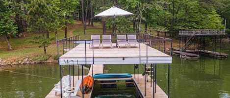 A wooden dock with a covered seating area, a boat, and a small bridge.
