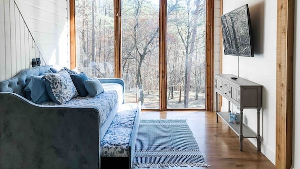 Un salon moderne avec un canapé, un téléviseur et une grande fenêtre donnant sur une forêt.