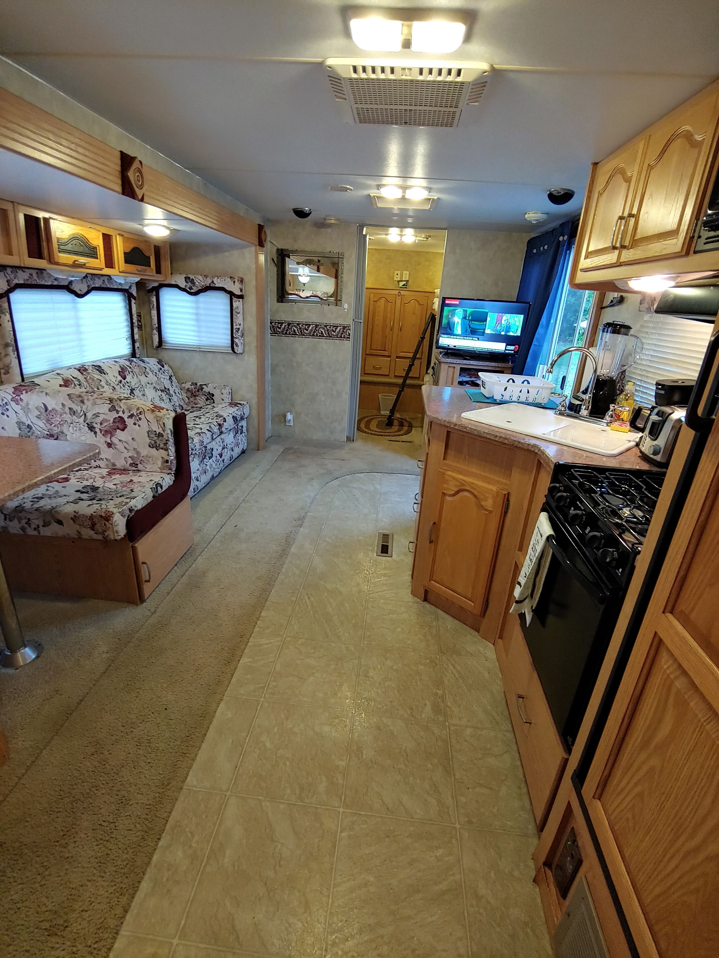 A compact RV kitchen with a central island, a dining area with a floral sofa, and wooden cabinets.