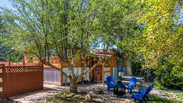 A backyard with a wooden fence, a tree, and outdoor furniture including blue chairs and a table.