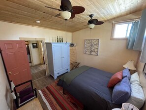 A bedroom with a bed, a wardrobe, a ceiling fan, and a window.