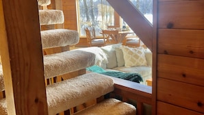 Un escalier en bois, dont les marches sont recouvertes de moquette, mène à une pièce d’où l’on peut admirer la vue sur les arbres à l’extérieur.