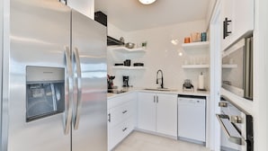 A modern kitchen with white cabinets, a stainless steel refrigerator, a dishwasher, and a built-in oven.