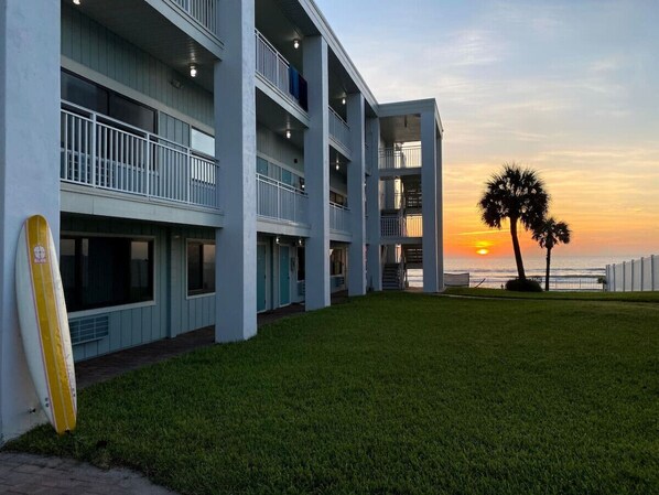 A multi-story building with balconies, a grassy lawn, and a sunset view. - Ocean View King Suite #211 (New Smyrna Beach)