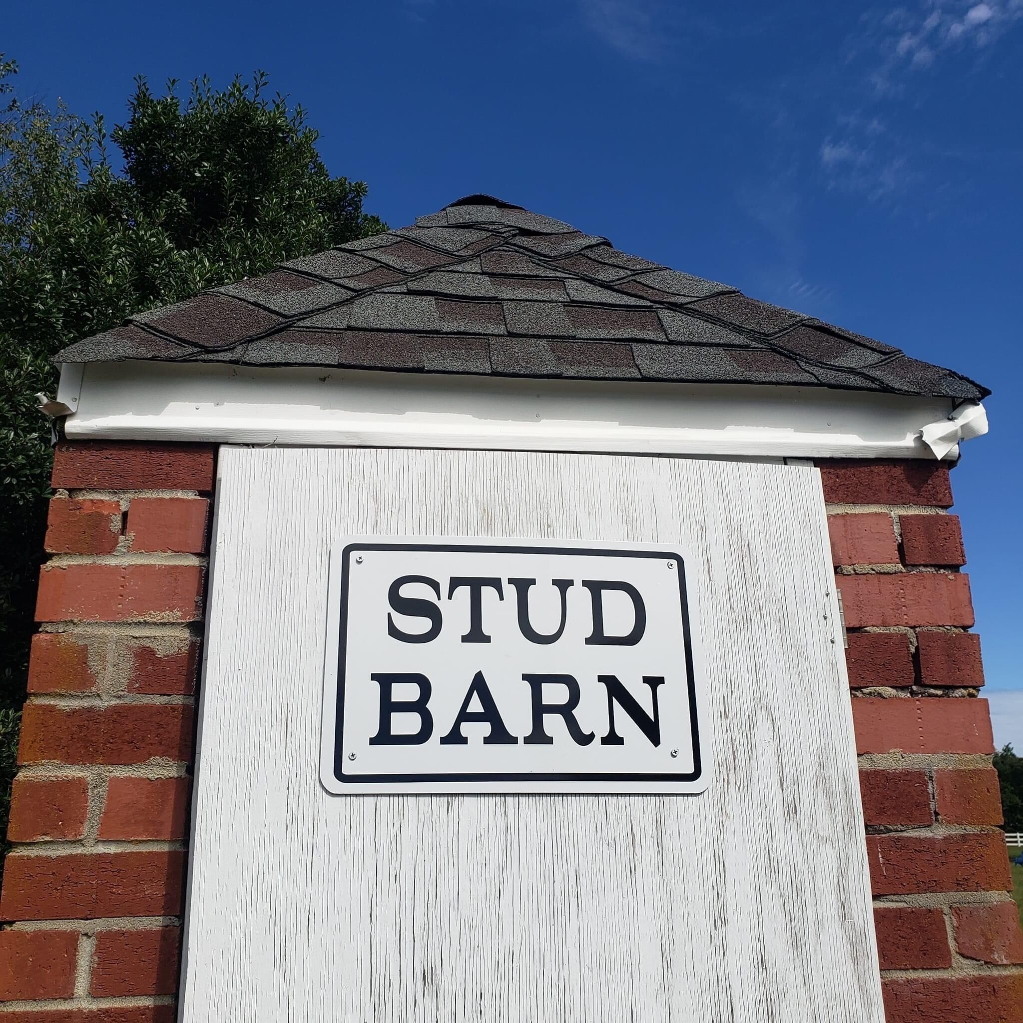 A sign reading "STUD BARN" mounted on a brick wall with a white trim and a dark roof.