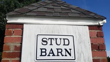 A sign reading "STUD BARN" mounted on a brick wall with a white trim and a dark roof.