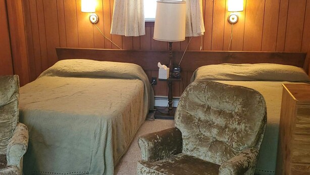Une chambre avec deux lits, une fenêtre avec des rideaux et des lampes fixées au mur.