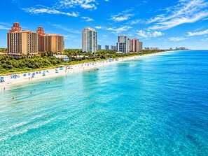 Un paisaje urbano costero con una playa, aguas azules cristalinas y edificios altos.