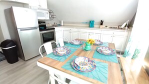 Eine kompakte Küche mit weißen Schränken, einem Edelstahlkühlschrank, einer Mikrowelle und einem Herd. Ein Esstisch mit bunten Tellern und eine Vase mit Blumen sind ebenfalls vorhanden.