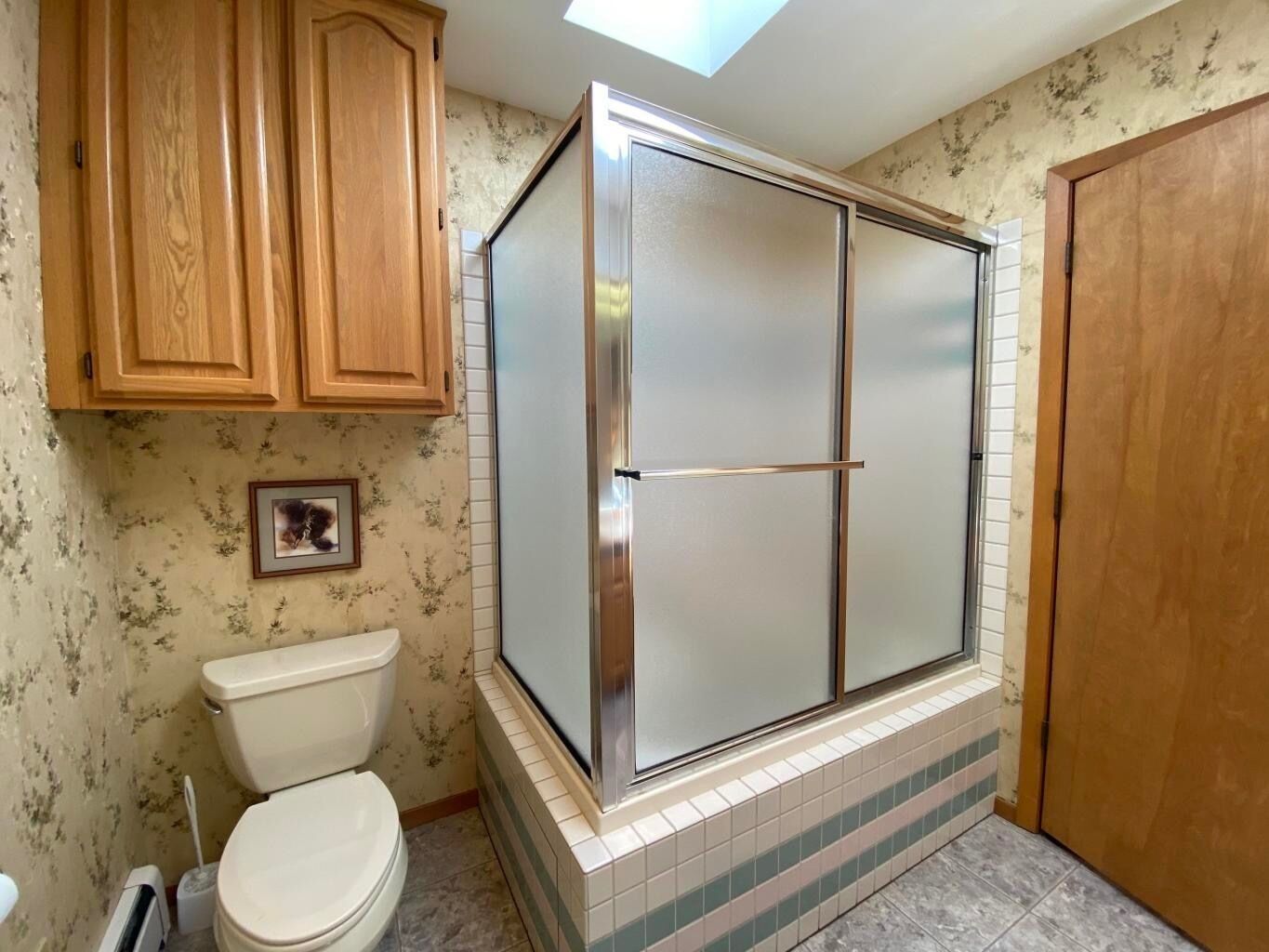 A bathroom with a toilet, wooden cabinets, a shower enclosure, and a skylight.