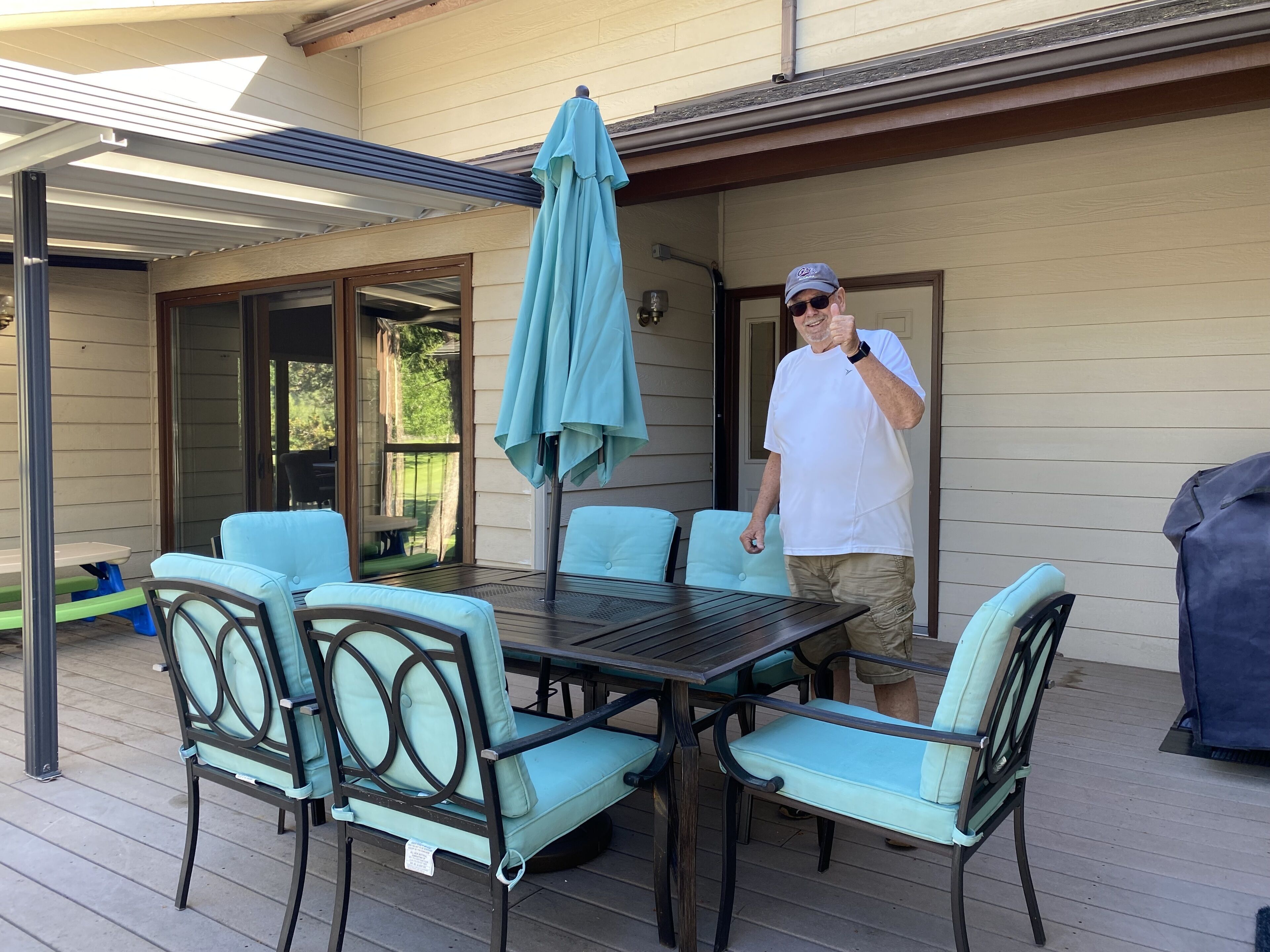 An outdoor patio with a table and chairs, a covered area, and a sliding glass door leading to a backyard.