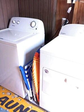 A laundry area with two white washing machines, a blue and orange striped item hanging, and a yellow floor mat with text. - Comfy Starfish,Fenced Backyard-ONLY 0.5mile to Beach-Sleeps 4-1BED/1.5BATH,2 TVs (Naples)