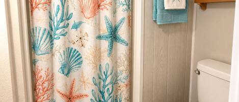 A bathroom with a shower curtain featuring a sea-themed pattern, a toilet, a blue rug, and a towel rack with a towel.