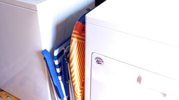 A front-loading washer and dryer in a laundry room with a wooden wall and a yellow floor mat with the word "LAUNDRY" visible.