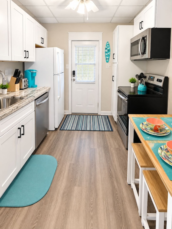 Cocina compacta con armarios blancos, microondas negro, refrigerador de acero inoxidable y cafetera color turquesa.