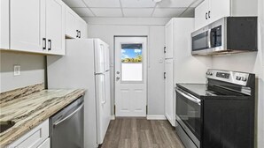 Una cocina compacta con alacenas blancas, microondas integrado, estufa y refrigerador.