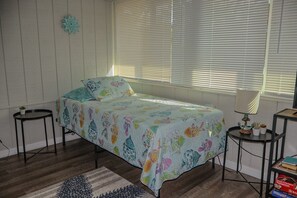A bedroom with a bed, two side tables, a lamp, a small plant, and a bookshelf.
