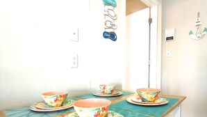 Un comedor con una mesa de madera y manteles individuales color turquesa, dos cuencos con diseños florales, y un cartel en la pared que dice "The Beach Is My Happy Place".