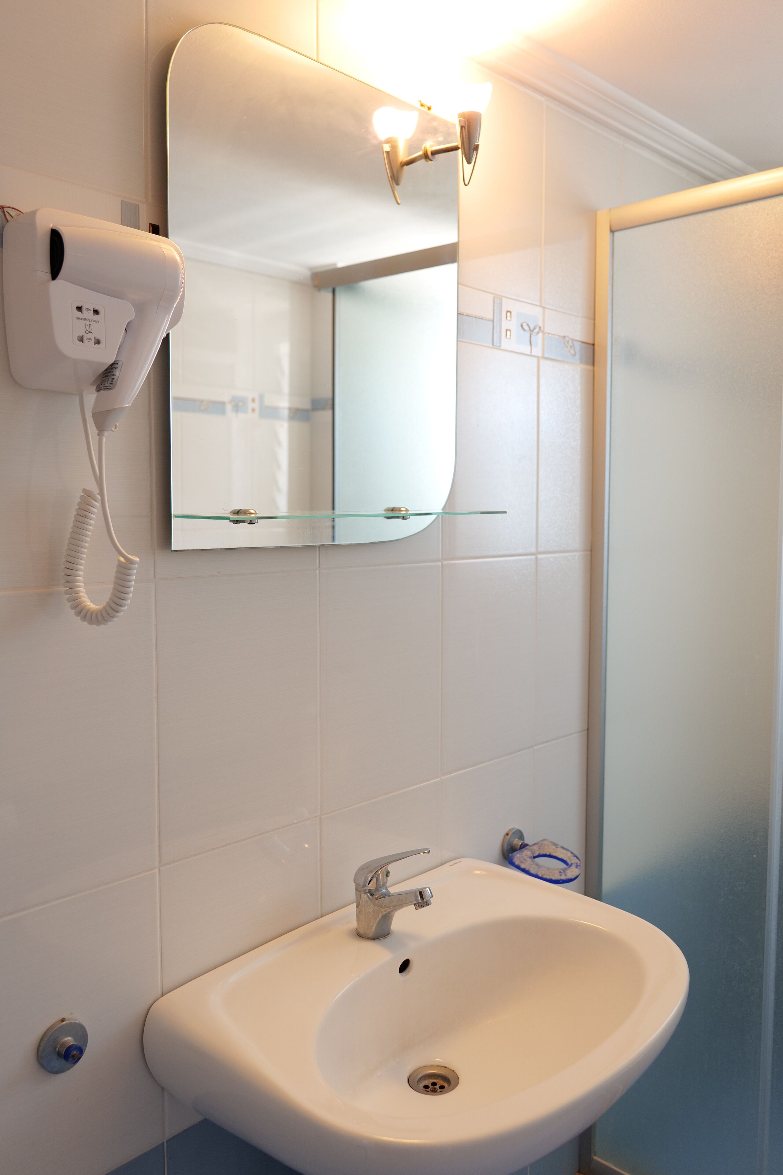 A bathroom with a white sink, a mirror, and a hairdryer on the wall.