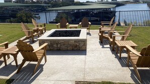 An outdoor seating area with Adirondack chairs and a stone fire pit, overlooking a body of water and buildings in the background. - Harborview FIRST FLOOR Condo w/ resort amenities easy poolside access w/ views! (Graford)