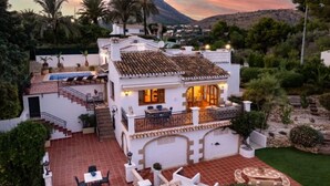 Uma casa de dois andares com varanda, área de estar ao ar livre e vista para a paisagem circundante.