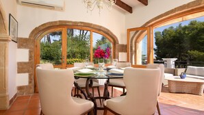 Uma sala de jantar com mesa posta para dois, ladeada por janelas arqueadas com vista para o verde.