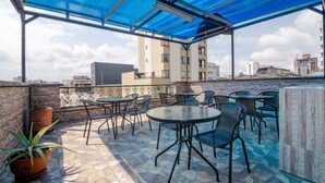 An outdoor patio with round tables and chairs, a blue canopy, and a view of buildings in the background. - Hotel Ayenda Olimpa 1144 (Pereira)