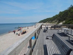 En træterrasse med udsigt over en strand med sandet bredde og en græsdækket bakke i baggrunden.