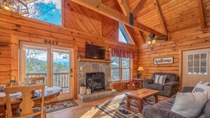 Un interior de cabaña acogedor, con chimenea de piedra, mobiliario de madera y un amplio ventanal con vistas panorámicas.