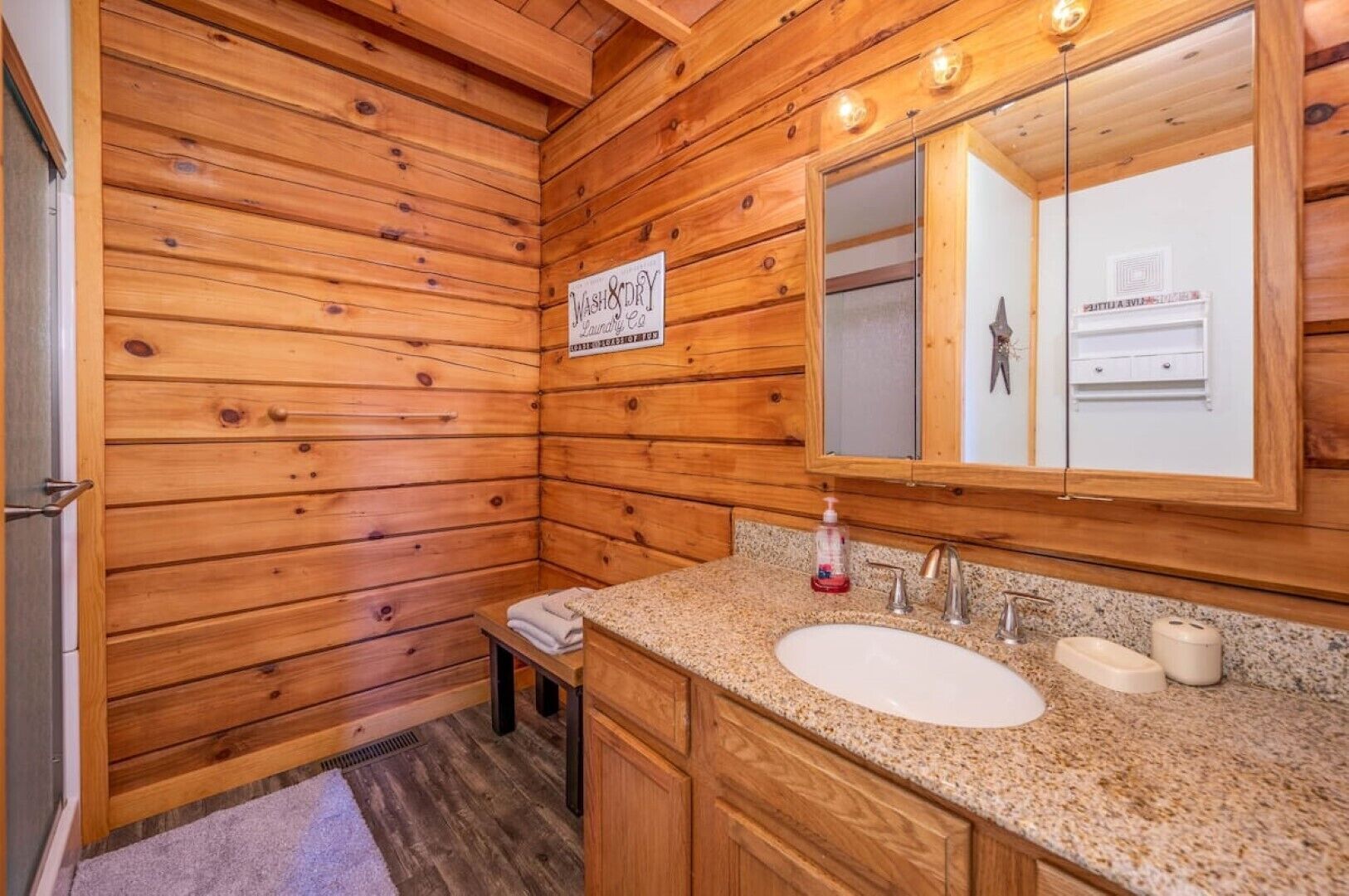 Une salle de bain rustique, aménagée dans une cabane en bois, avec un lavabo, un miroir et un panneau indiquant qu’il s’agit d’un espace où l’on peut se laver et se sécher.
