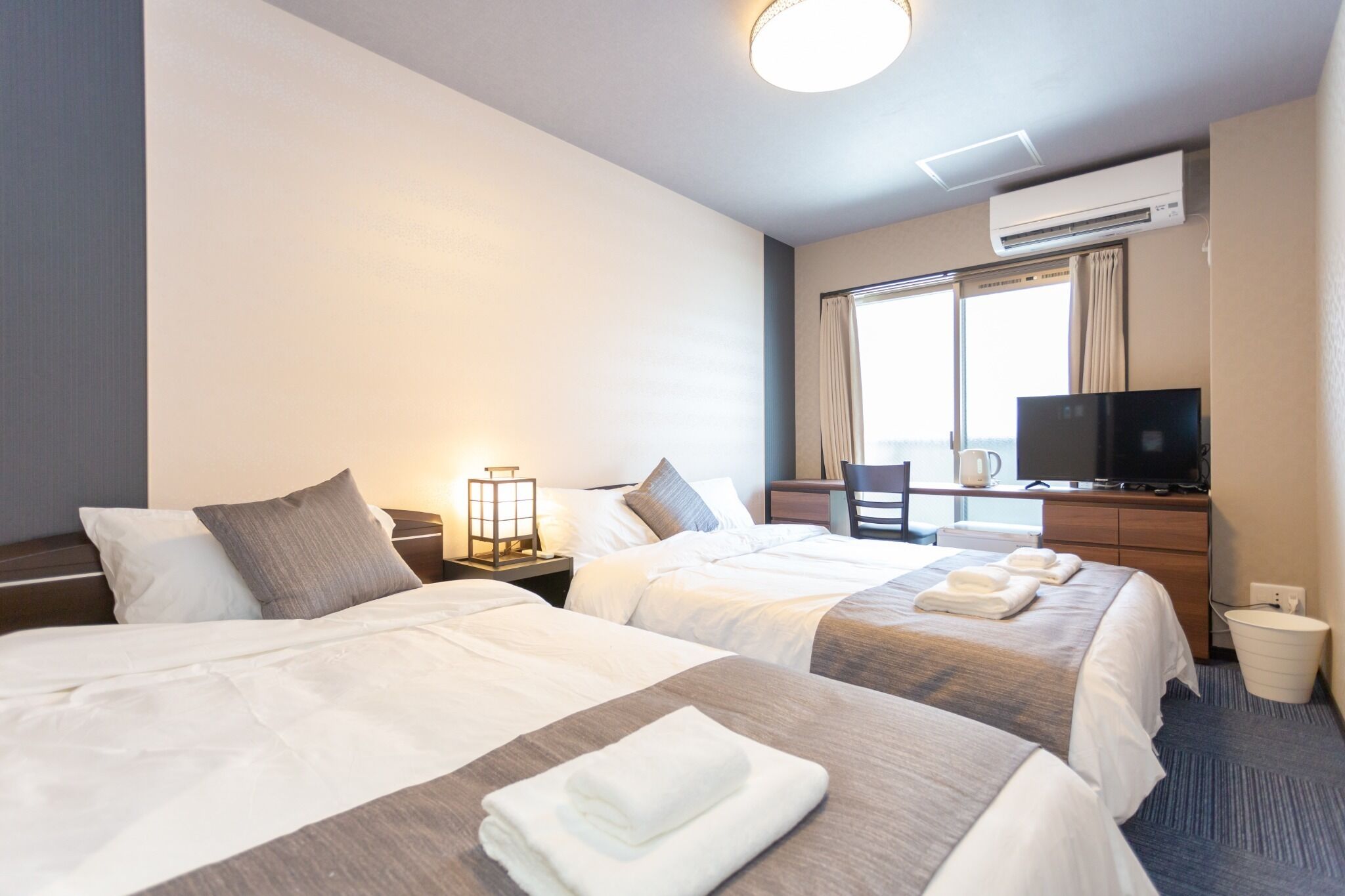 A hotel room with two beds, a desk with a television, and a window with curtains.