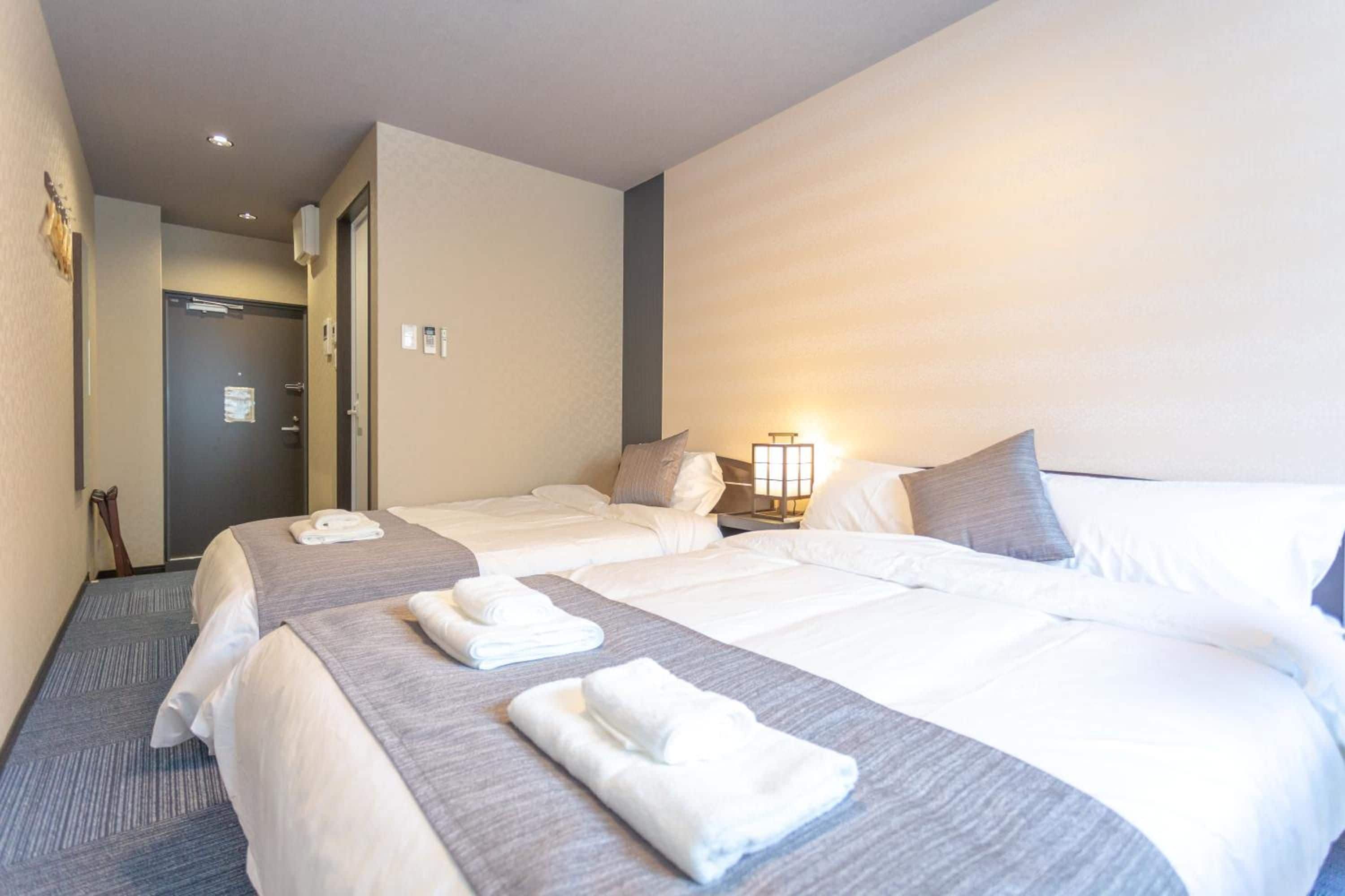 A hotel room with two beds, a door, and a nightstand with a lamp.
