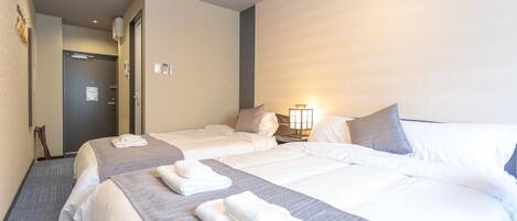 A hotel room with two beds, a door, and a nightstand with a lamp.