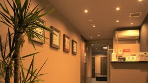 A hallway with a potted plant, framed artwork on the wall, and a reception desk with a sign. - SlowTime Hotel Kyoto (Kyoto)