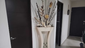 Een hal met een decoratieve plantenstandaard, een deur en een donkerdeur op de achtergrond.