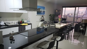 Een moderne keuken met een zwart aanrecht, witte kasten en een bar met krukken. Er is een raam met uitzicht op gebouwen en een stadsgezicht.