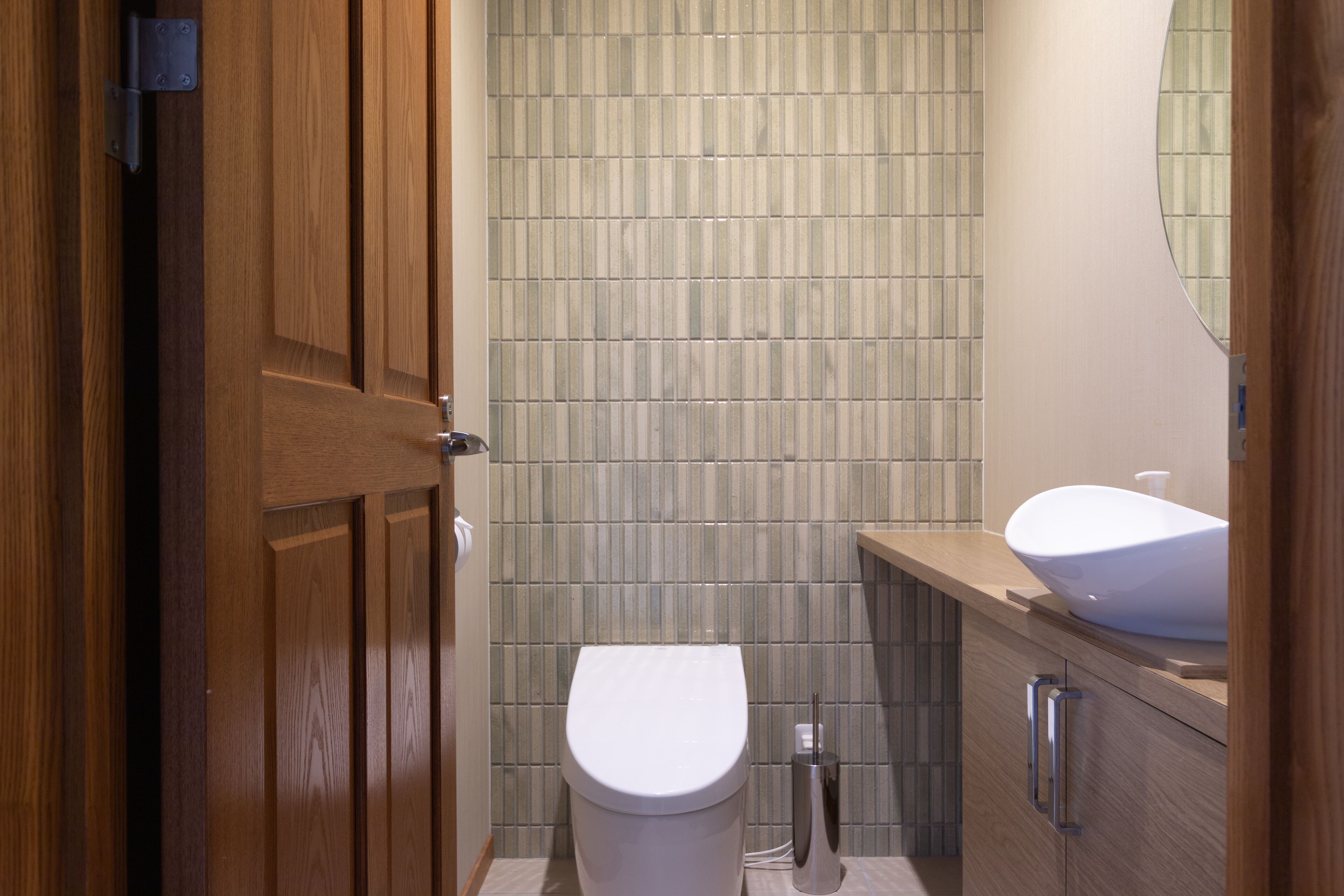 Une salle de bain avec une porte en bois, des toilettes, un lavabo et un mur carrelé.