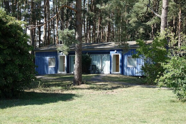 Une cabane bleue avec deux portes ouvertes, entourée d’arbres et d’herbe.